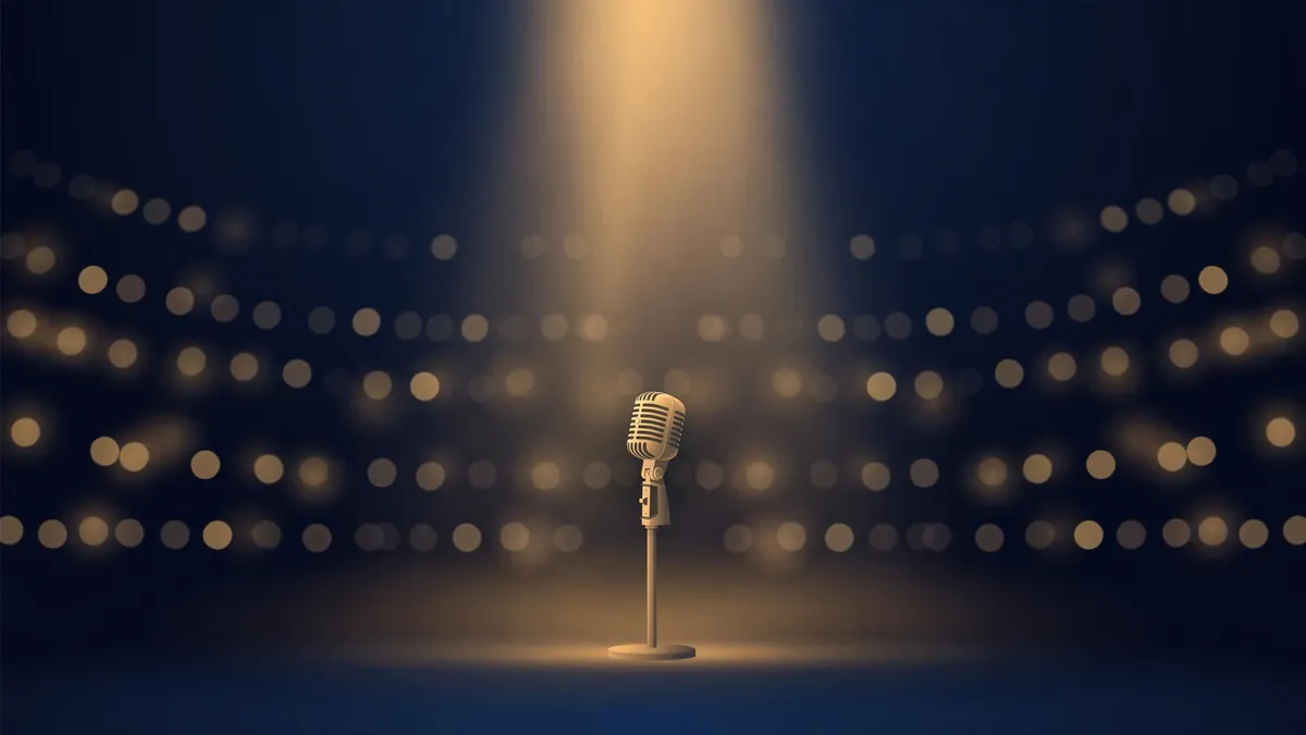 A lone microphone on a stand under a single gold spotlight in a dark comedy arena, navy and gold editorial illustration