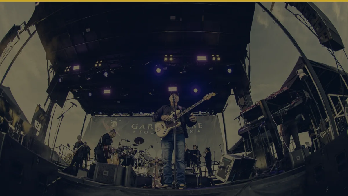 Gary Sinise performing with the Lt. Dan Band at Camp Johnson, Vermont, in September 2026, in a navy and gold duotone treatment